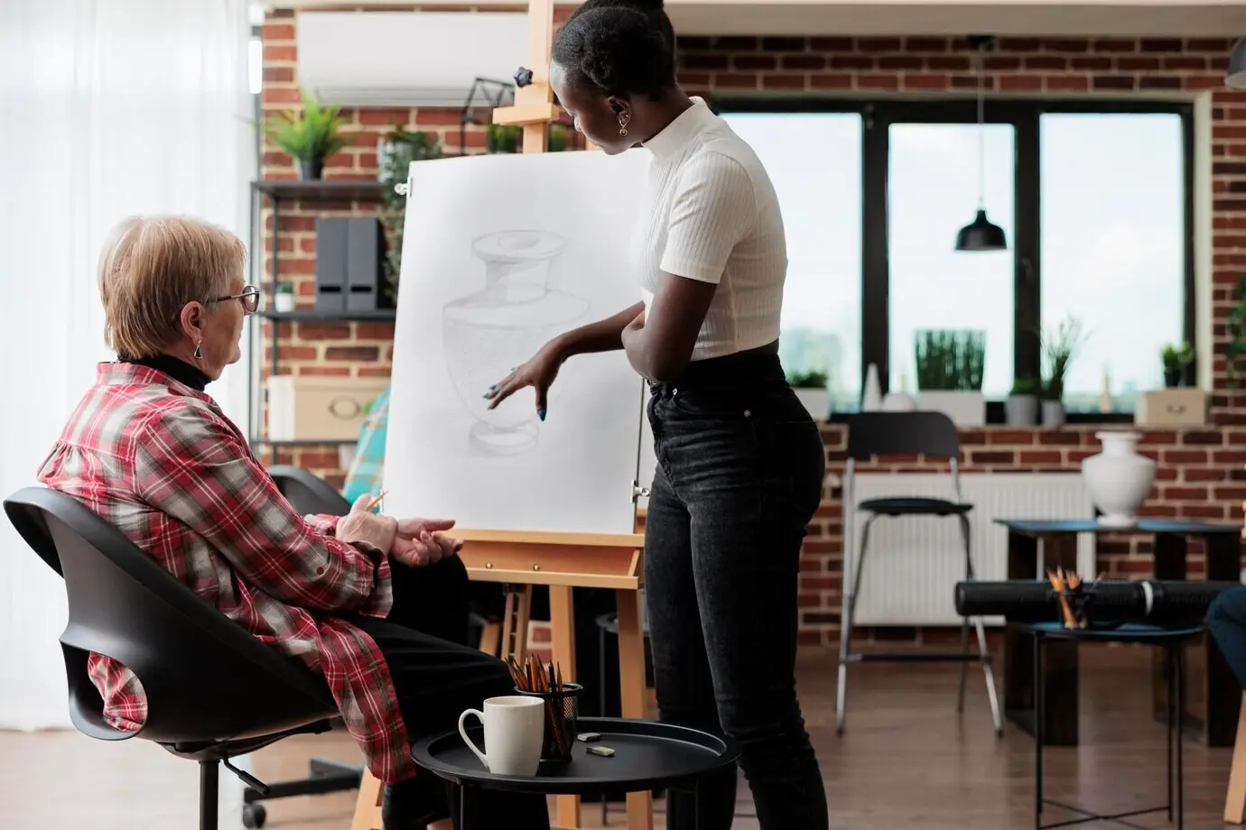 Afroamerikanische Kunstlehrerin erklärt einem älteren Schüler während eines Kreativkurses eine Zeichentechnik. Eine Künstlerin skizziert auf weißer Leinwand ein Vasenmodell mit einem Zeichenstift. Neujahrsvorsätze.